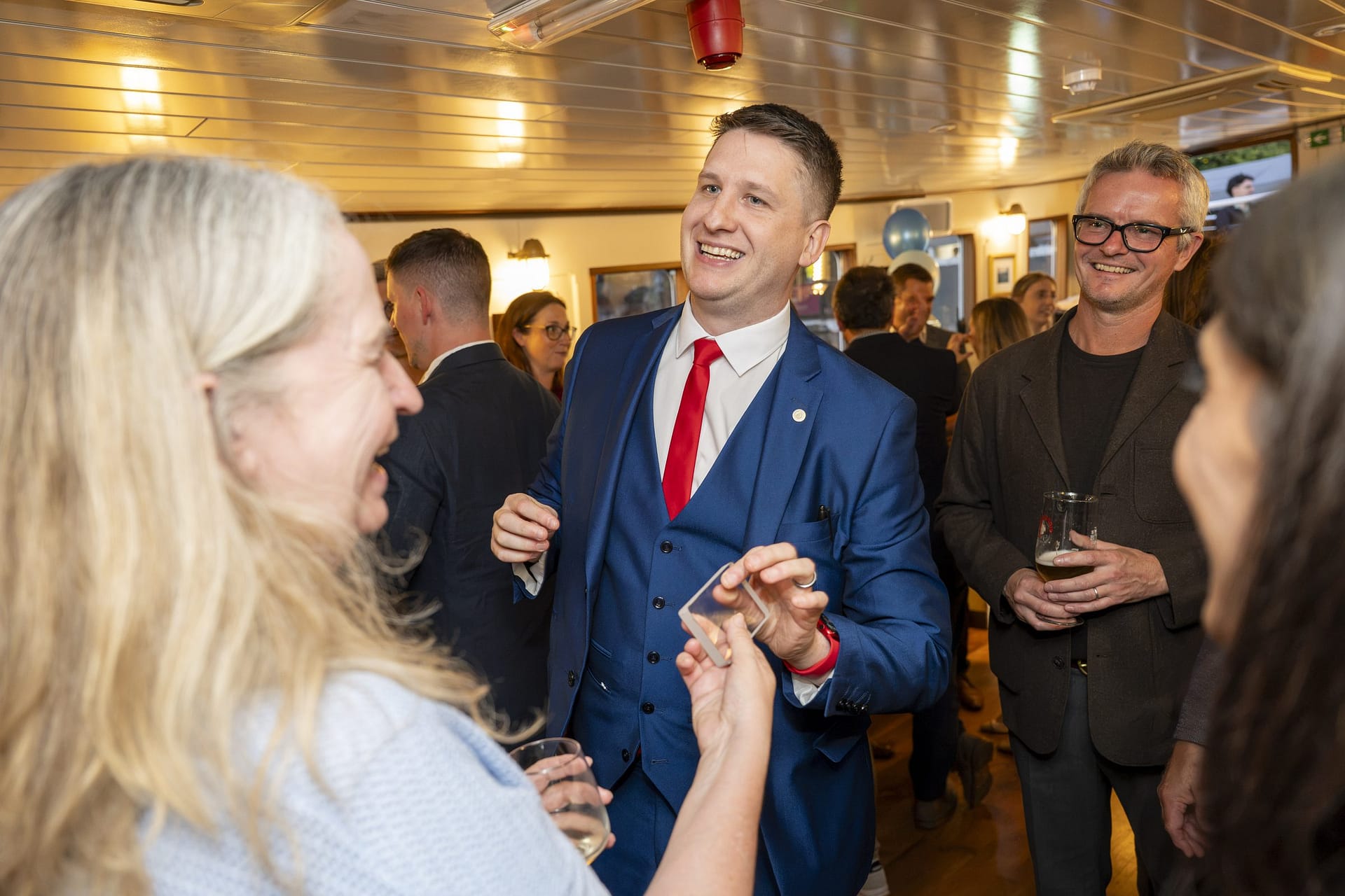 Pete James performing close-up magic for laughing guests at a Thames boat party in London
